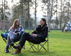 two women sitting on camping chairs on an open camping field. 