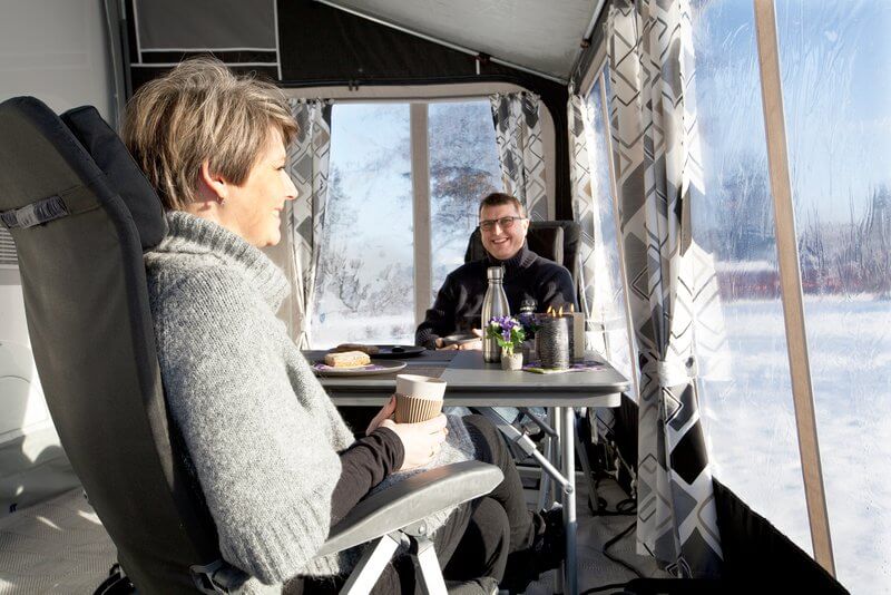 A photo of a couple sat having a hot drink in their all season awning on a winters morning with snow outside. 