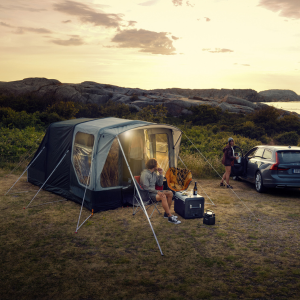 an image of a tent positioned on the side of the hill sea scene at dusk. There is a car parked off the corner of the scene with a person getting out. 