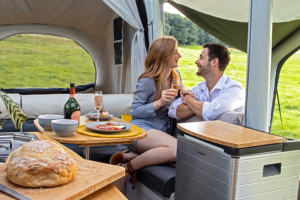 an image showing a couple inside the opus self inflating trailer tent enjoying a bottle of fix and homemade bread on a summers day. 