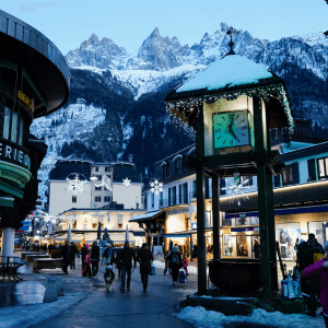 a scene depicting a village in the snowy mountains, a clock tower at the forefront with Christmas decorations and lights